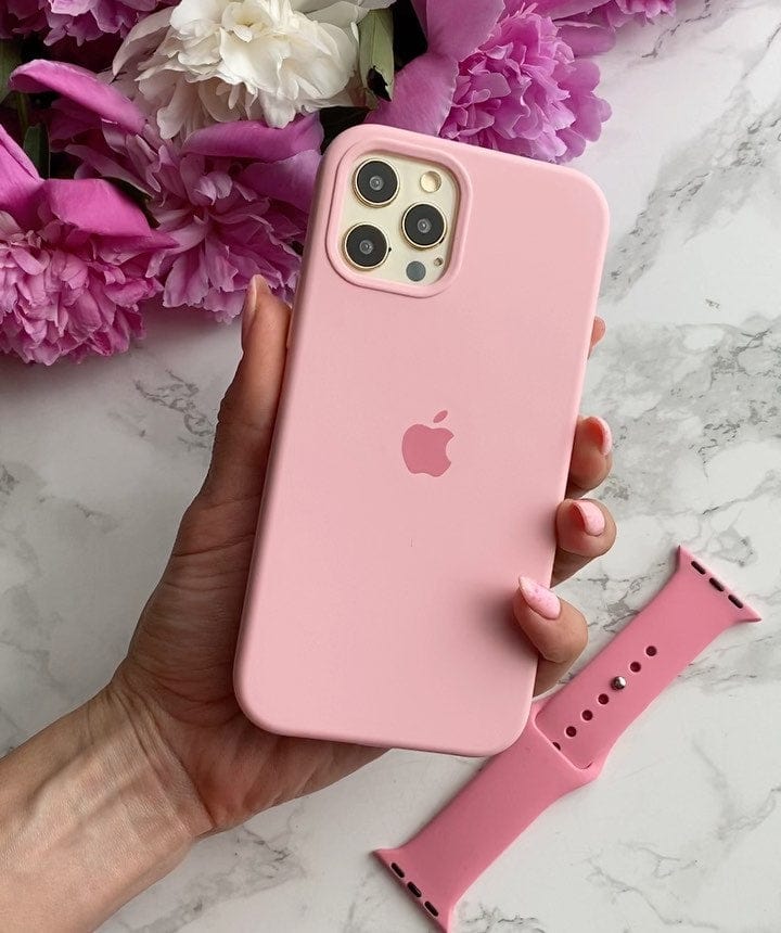 Hand holding a triple-camera iPhone in a candy pink silicone case beside flowers and a pink watch band.