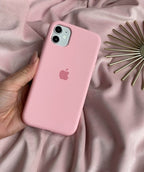 Hand holding a dual-camera iPhone in a candy pink silicone case against pink fabric.