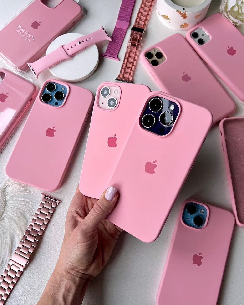 Hand holding two iPhones in candy pink silicone cases beside matching cases and watch bands.