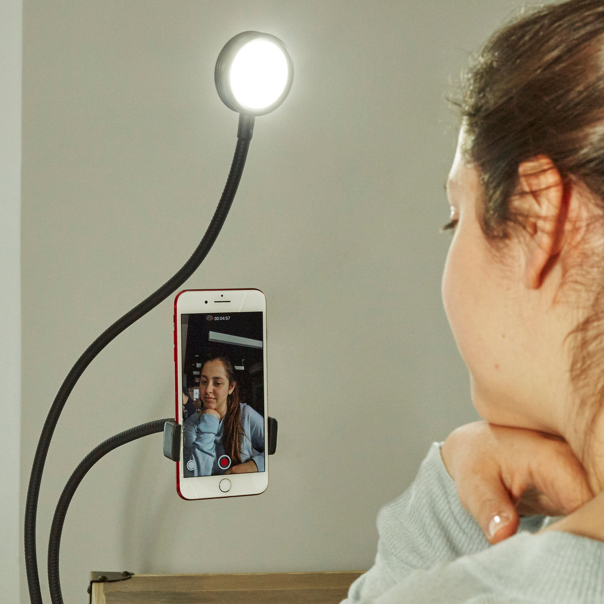 Woman recording with a phone mounted vertically beside the live streaming kit illuminated LED light.