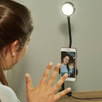 Woman waving at a vertically mounted phone with the live streaming kit LED light above it.