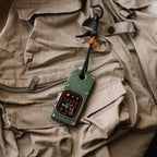 Olive green miniPhone Ultra case and Apple Watch Ultra secured to a tan vest with a cord and clip.