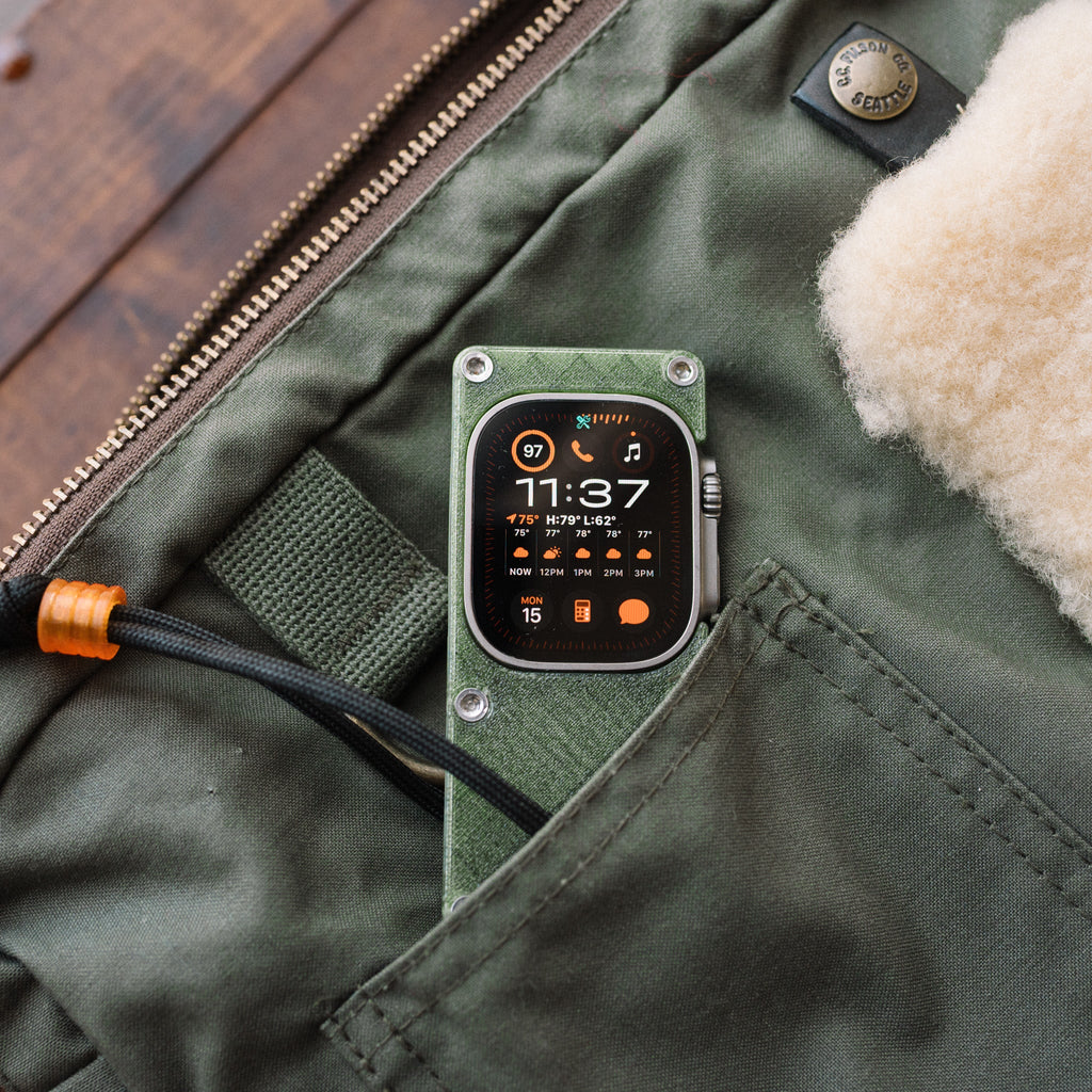 Close-up of Apple Watch Ultra in an olive green miniPhone Ultra case inside a green jacket pocket.