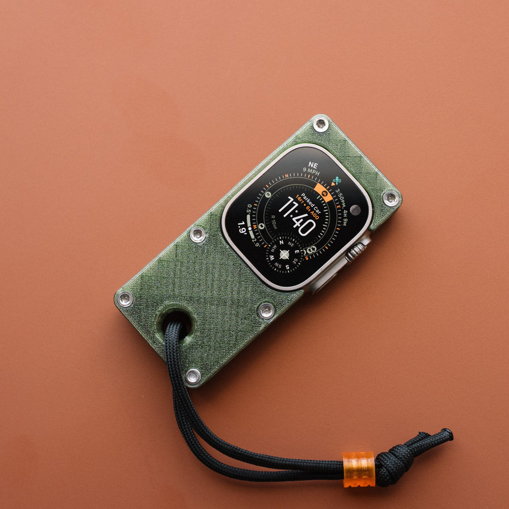 Apple Watch Ultra in an olive green miniPhone Ultra case with a black cord on an orange background.