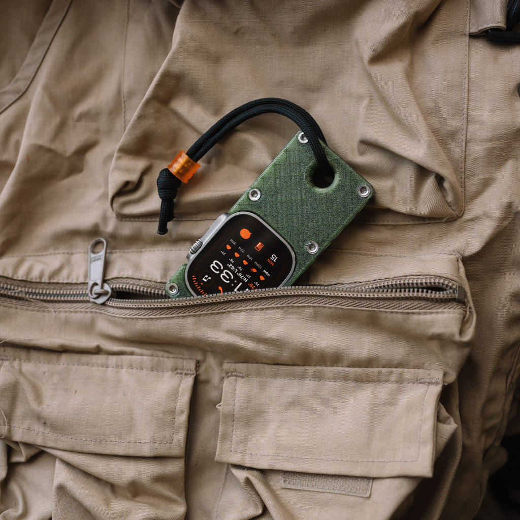 Olive green miniPhone Ultra case holding an Apple Watch Ultra at the opening of a tan vest pocket.